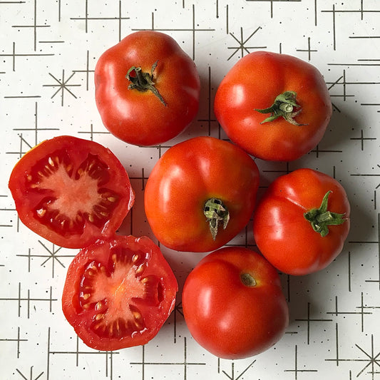 Six round red tomatoes with one cut in half to display its interior.