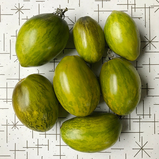 Seven light green roma shaped tomatos with dark green stripes.