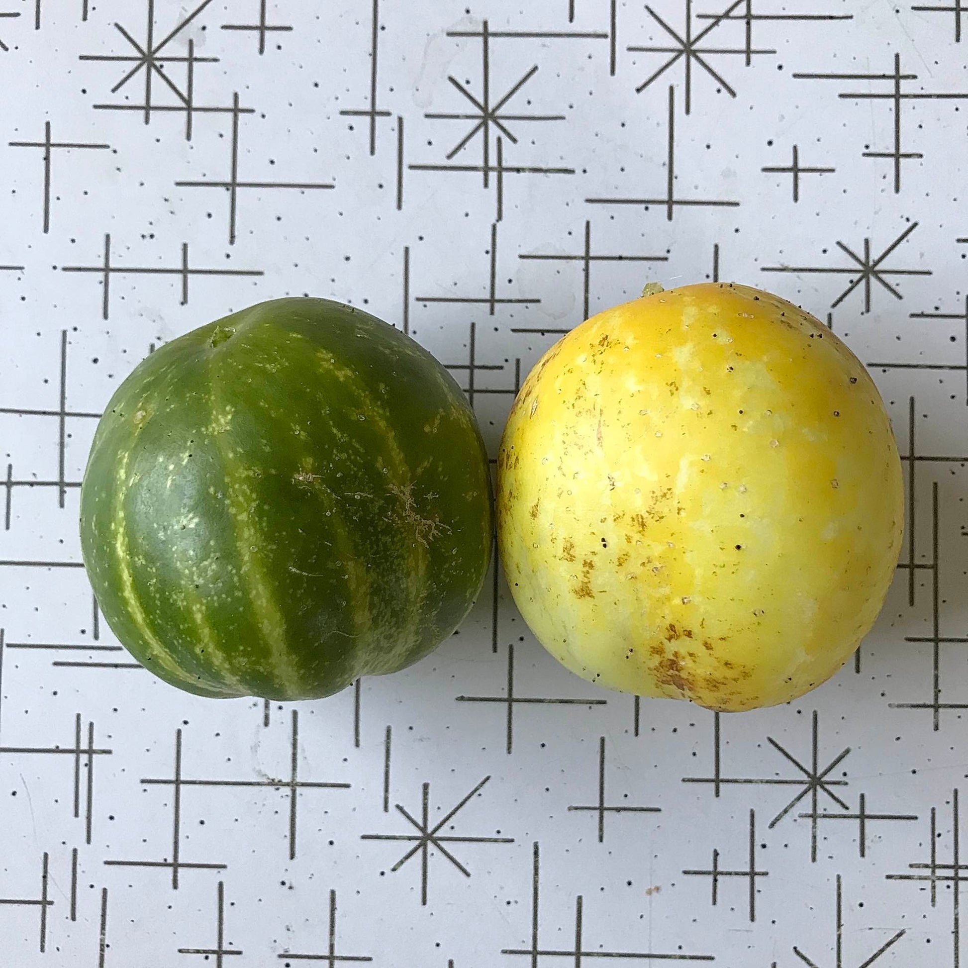A lemon cucumber and a lime cucumber side by side on a table.