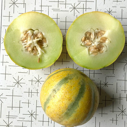 Striped galia melon cut in half, next to a whole melon.