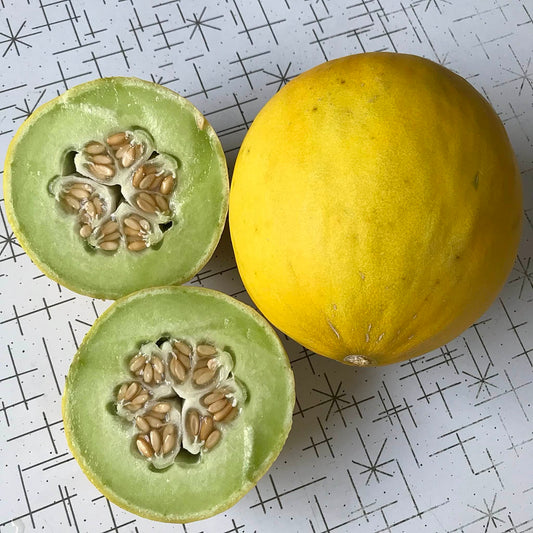 Golden honeydew melon with green flesh cut in half next to a whole melon.