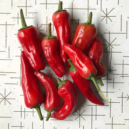 Pile of small triangular hot peppers at peak ripeness on a table.