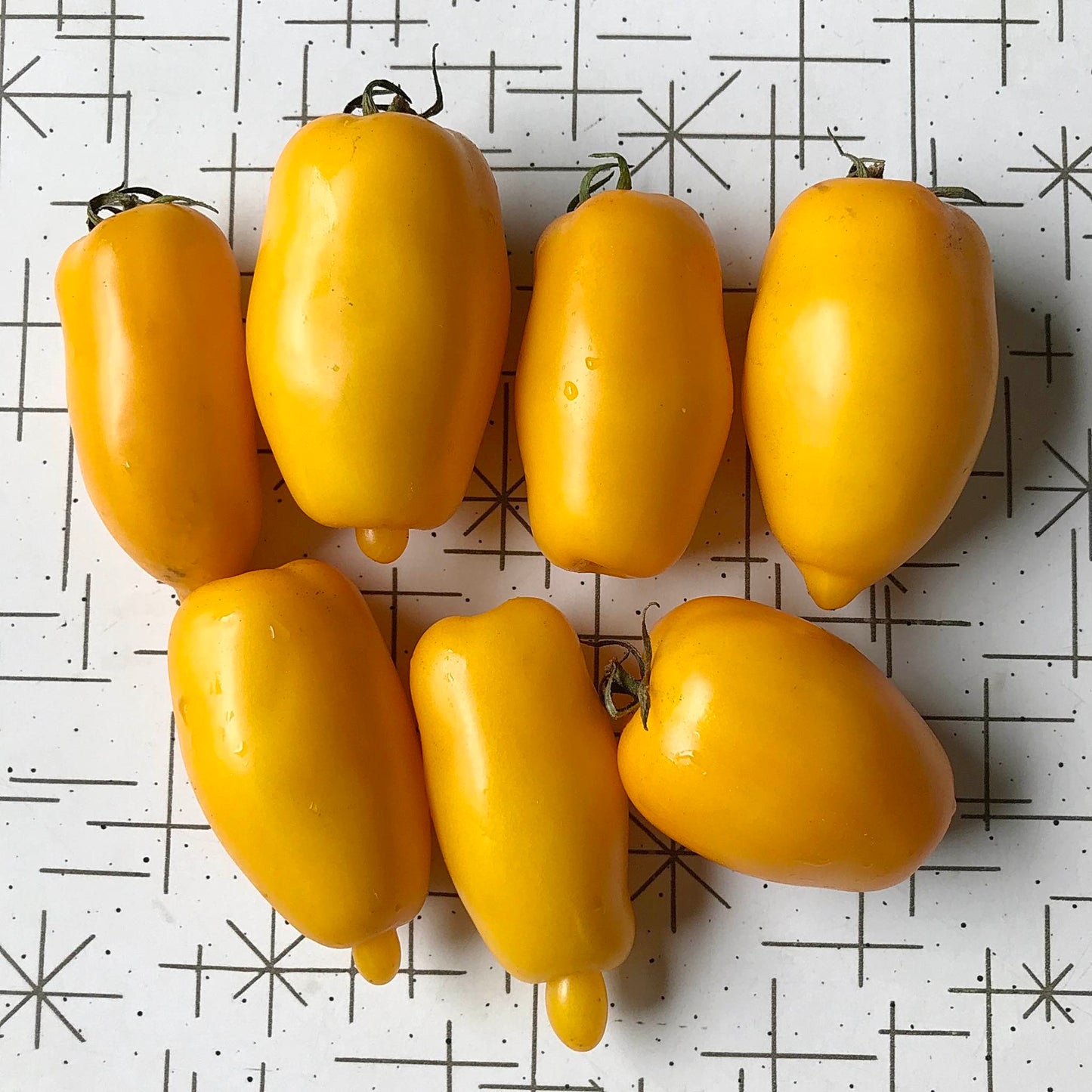 Seven yellow roma tomatoes on a table.