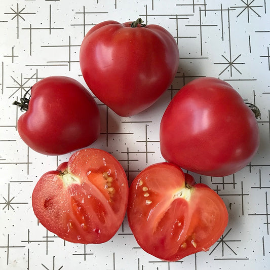 Four heart shaped tomatoes, one cut in half to display its interior.