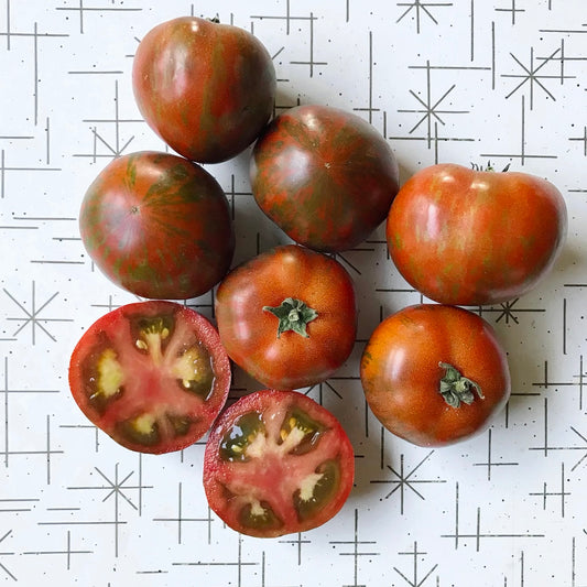 Seven round red tomatoes with green stripes, one cut in half to display its interior.