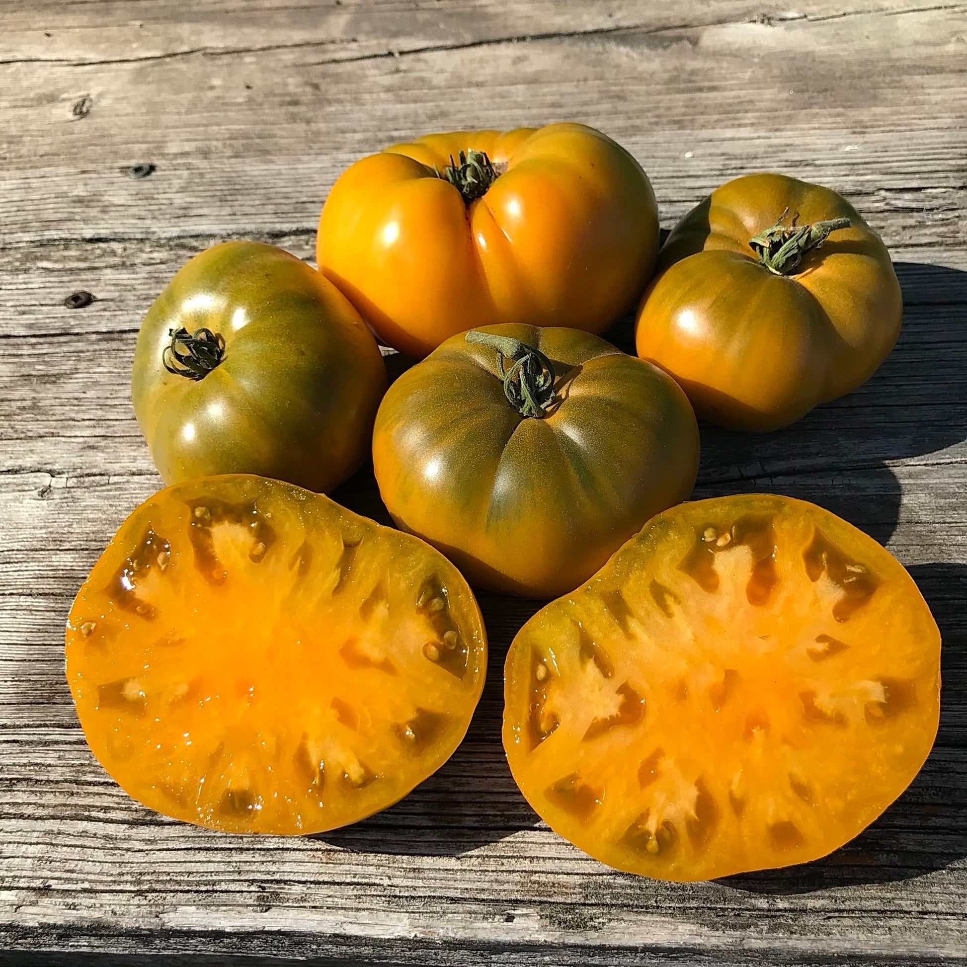 Orange tomatoes with olive green shoulders sitting on an old porch step. 