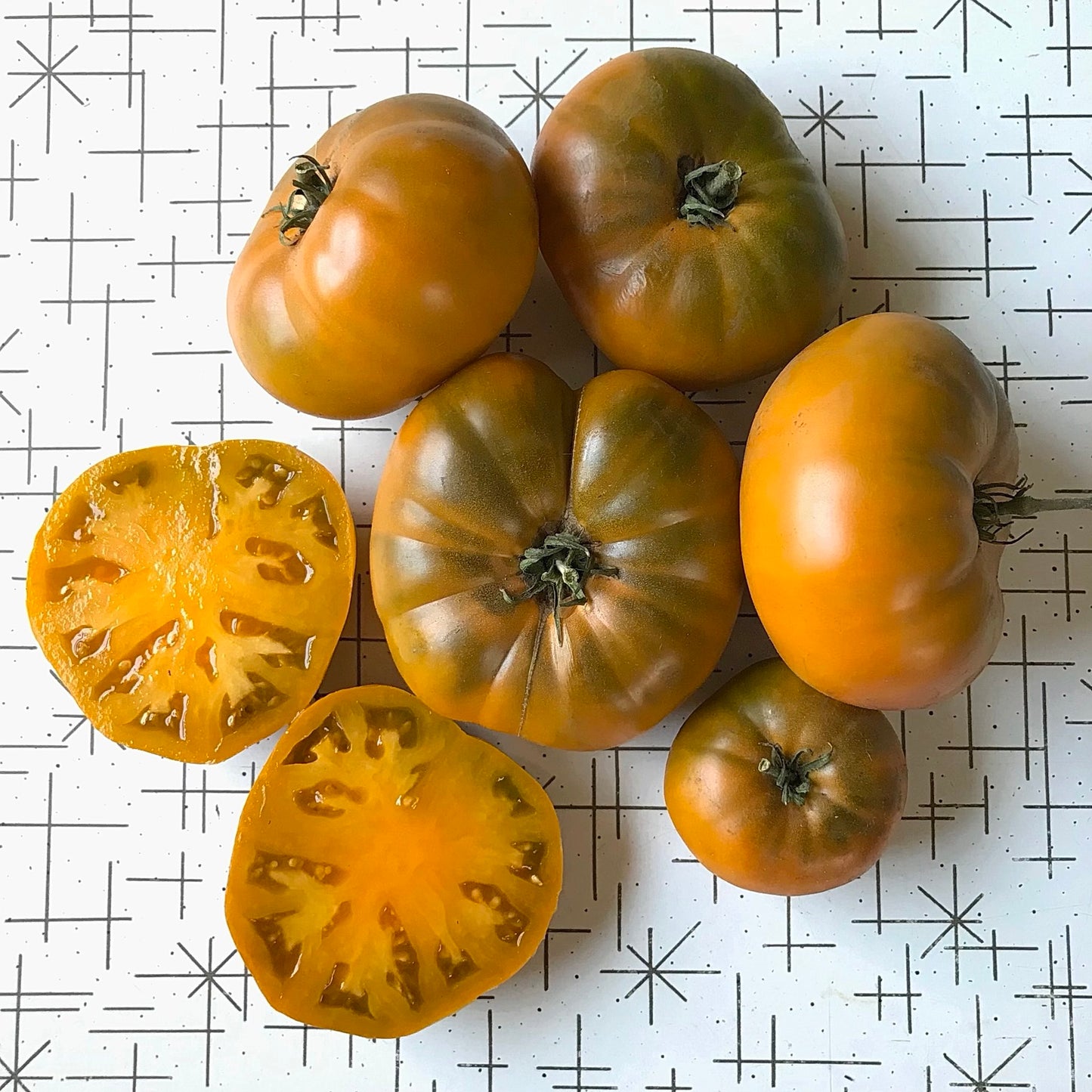 Orange beefsteak tomatoes with olive green shoulders, one cut in half to display its interior.