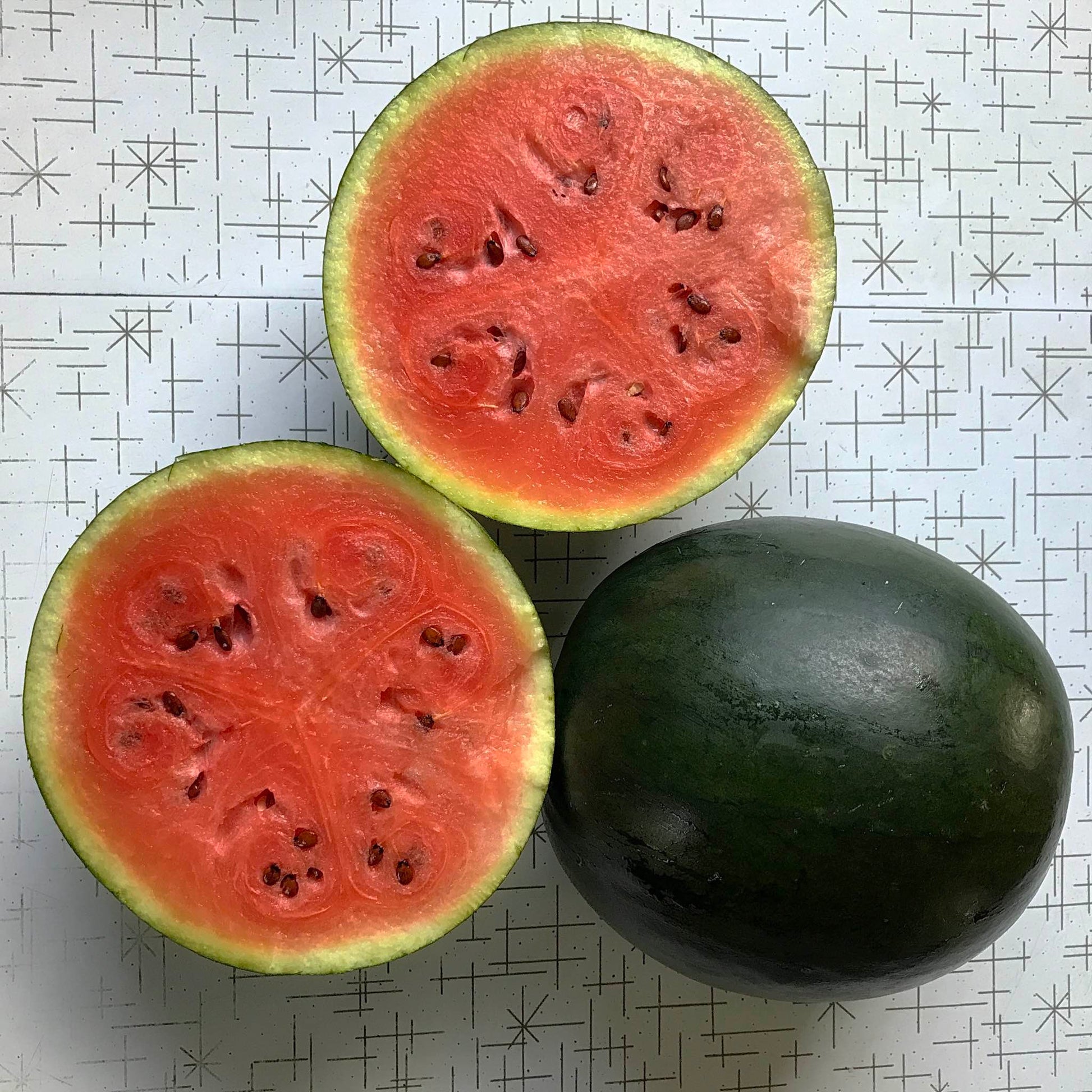 Whole dark green watermelon beside one cut in half to display its interior.